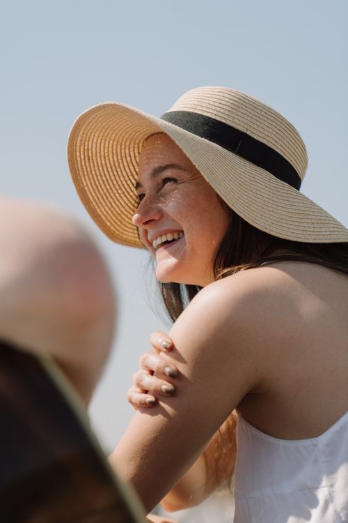 Free A cheerful woman with freckles and a sun hat smiles outdoors, enjoying a sunny summer day. Stock Photo