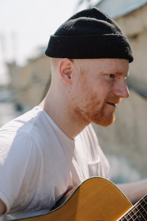 Man in White Crew Neck T-shirt and Black Knit Cap Holding Brown Acoustic Guitar