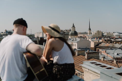 Man in White Tank Top and Brown Hat Standing on Roof Top