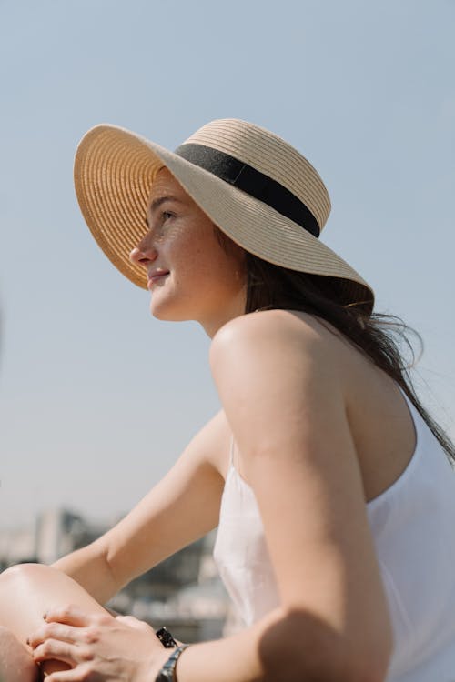 Женщина в белом платье с открытыми плечами и коричневой соломенной шляпе