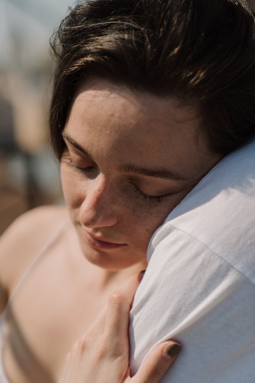 Free Young woman with eyes closed, tenderly embracing someone outdoors, reflecting love and serenity. Stock Photo