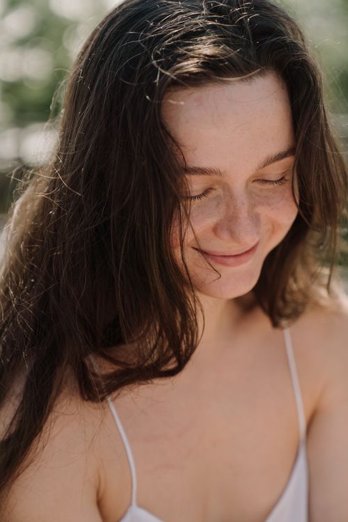 Free A smiling woman with long hair enjoying a sunny day outdoors. Stock Photo