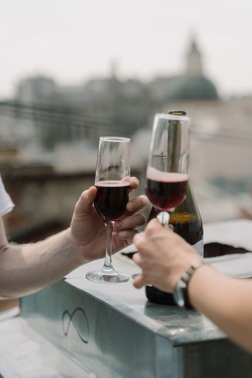 Free Cheerful couple toasting with red wine on a scenic rooftop, creating a romantic moment at sunset. Stock Photo