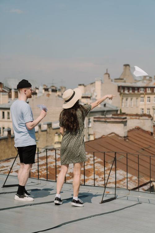 Free A couple relaxing on a rooftop, throwing a paper airplane with a cityscape view. Stock Photo