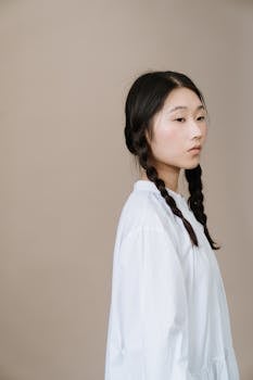 Profile portrait of a young woman with braided hair against a beige background.