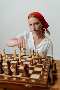 一位戴着红头巾的红发女子正在室内的木制棋盘上下棋