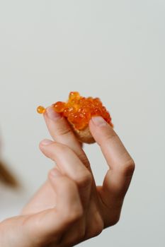一只手持着一片撒有红色鱼子酱的面包，以特写镜头展现了俄罗斯美食的风味