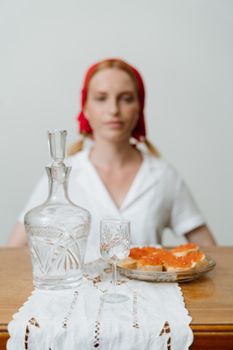 红发女人的背景前，桌上摆着水晶酒瓶和面包