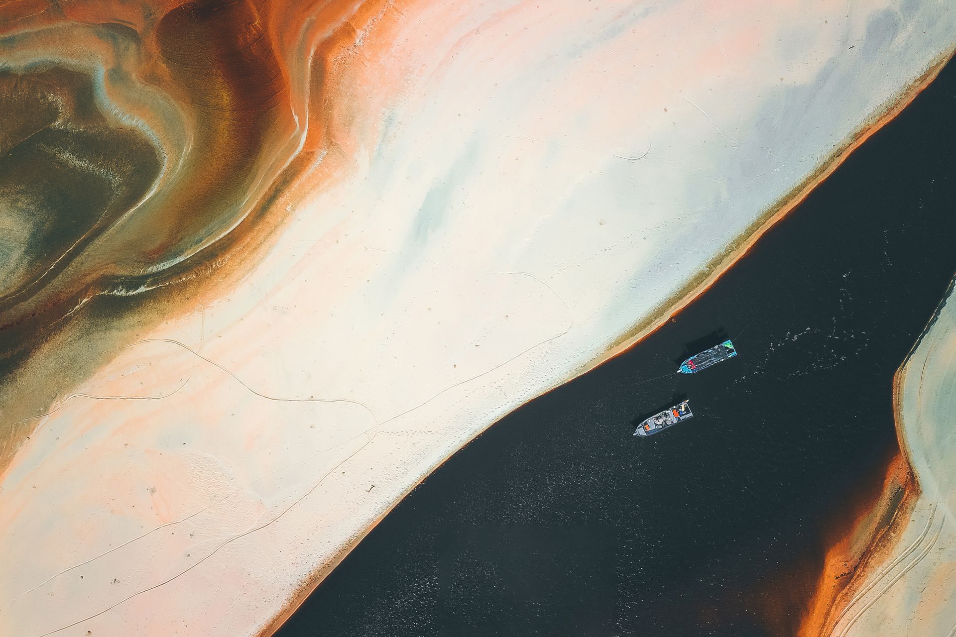 Aerial view of colorful textured sandy shore near floating boats in water in sunny day