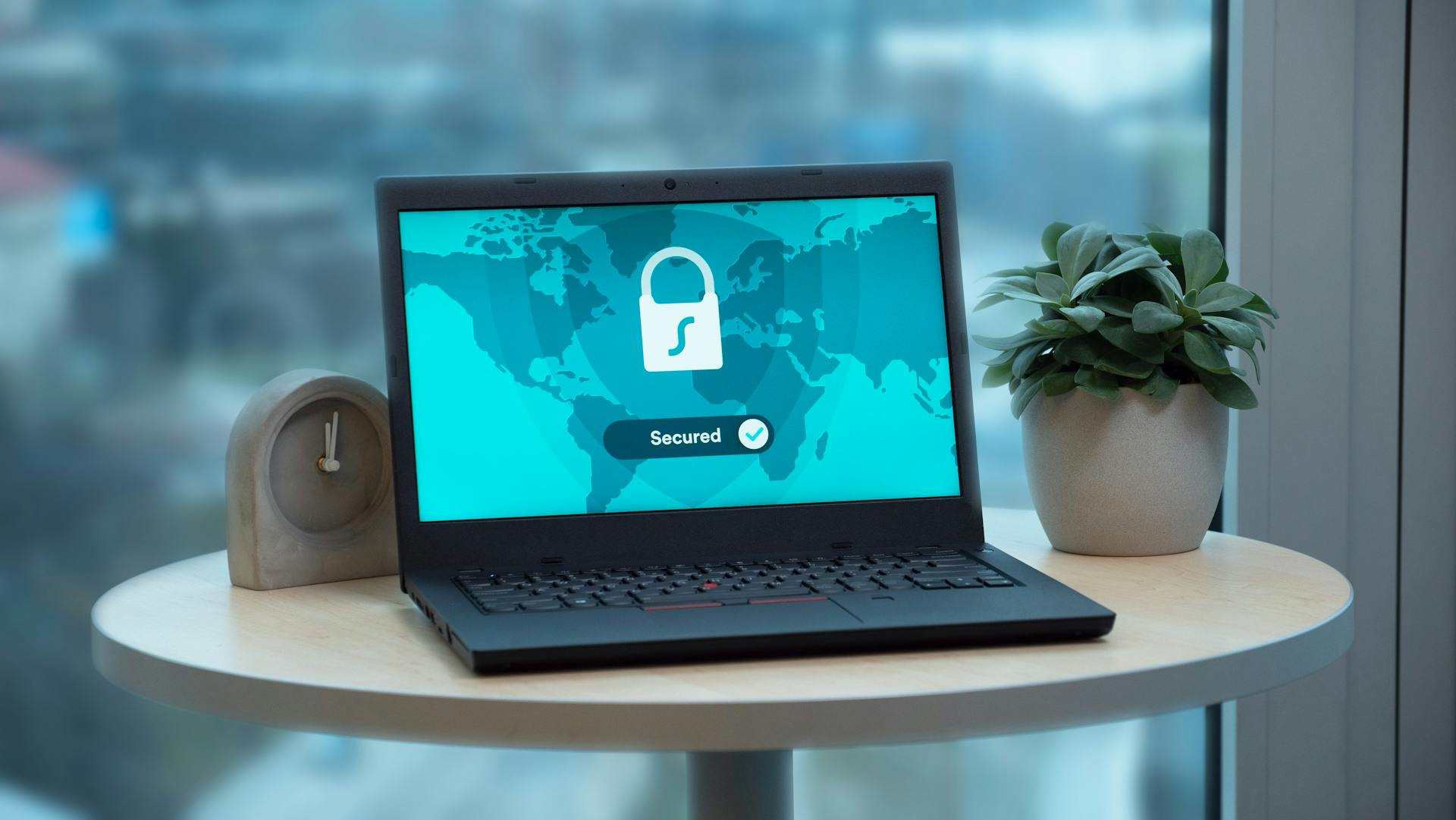 Laptop displaying a security lock icon on a table with a potted plant and clock.