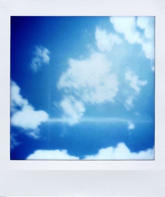 Soft focus Polaroid of blue sky with fluffy white clouds, creating a dreamy effect.
