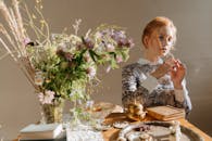 一位红发女子优雅地坐在桌前，桌上摆满了野花和复古装饰
