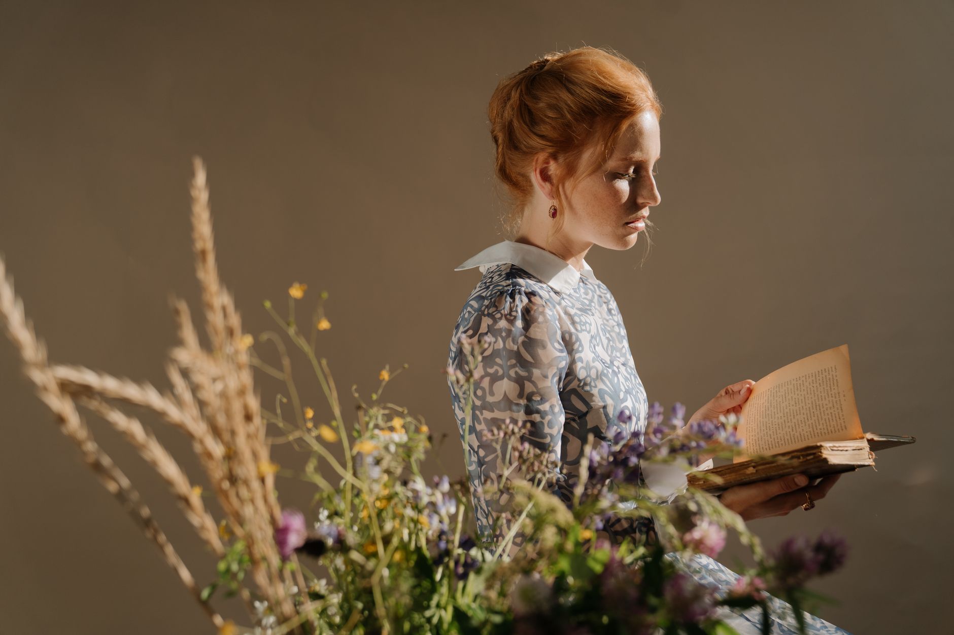 Redheaded woman elegantly reading an open book among wildflowers, embodying noble Russian style.