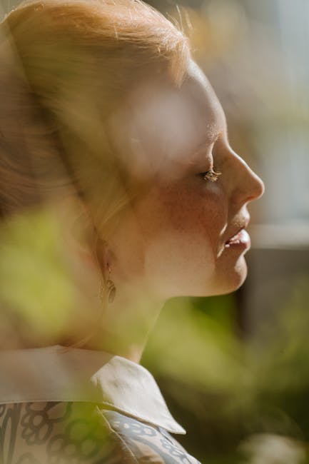 Profile of a redheaded woman with freckles, gracefully lit by sunlight, conveying elegance and serenity.