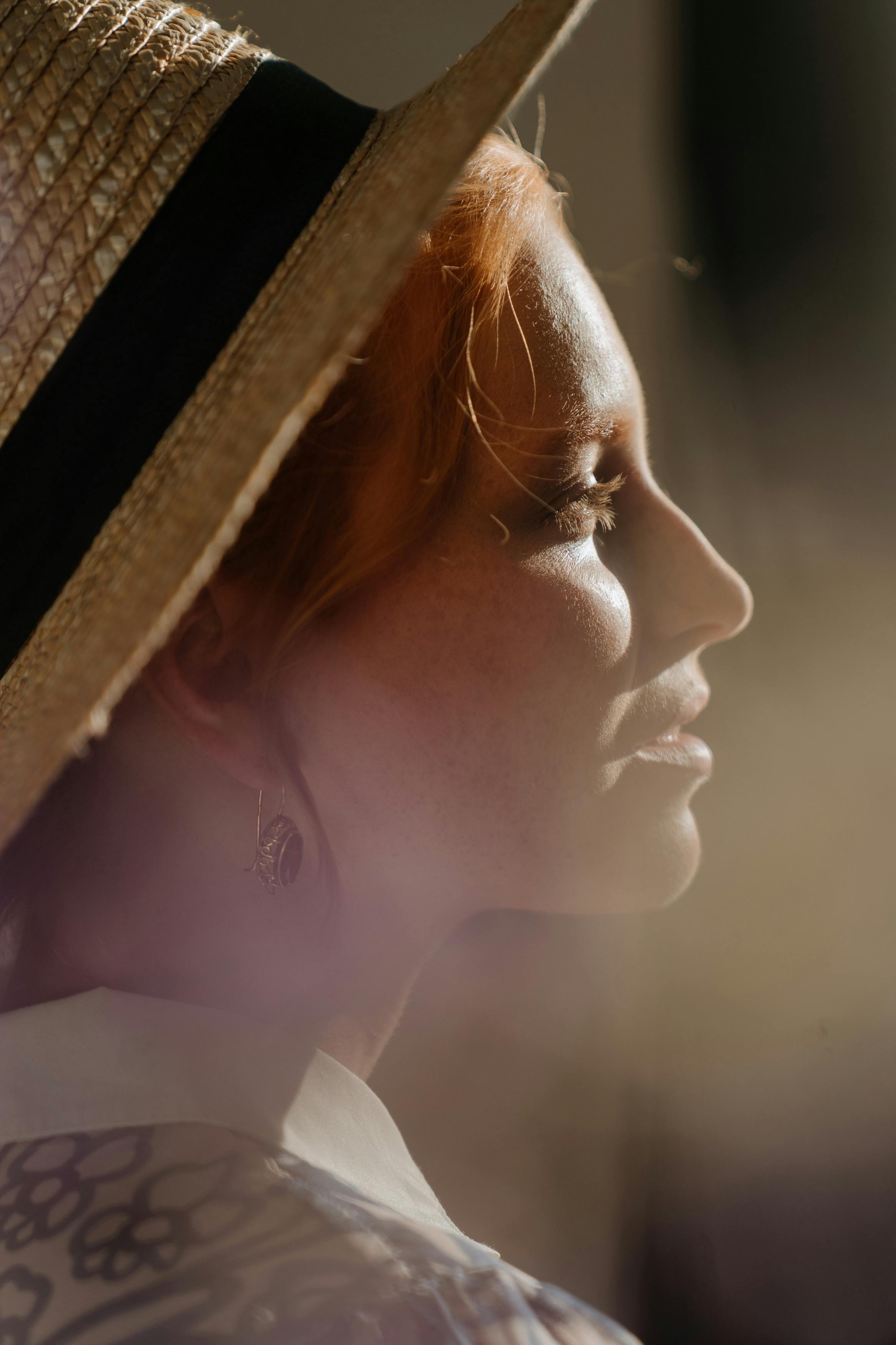 Profile of a redheaded woman wearing a straw hat, bathed in warm sunlight.