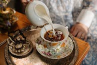 在复古茶场景中，牛奶被倒入洋地黄茶，周围点缀着珍珠和华丽的珠宝