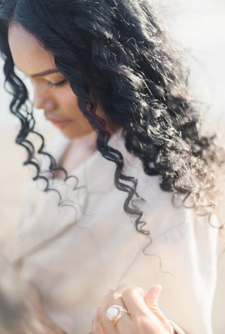 From above side view of crop trendy contemplative ethnic female with curly hair and ring on finger looking down in back lit