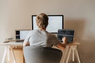 Back View of a Boy Sitting on Grey Chair while Using His Laptop Computers