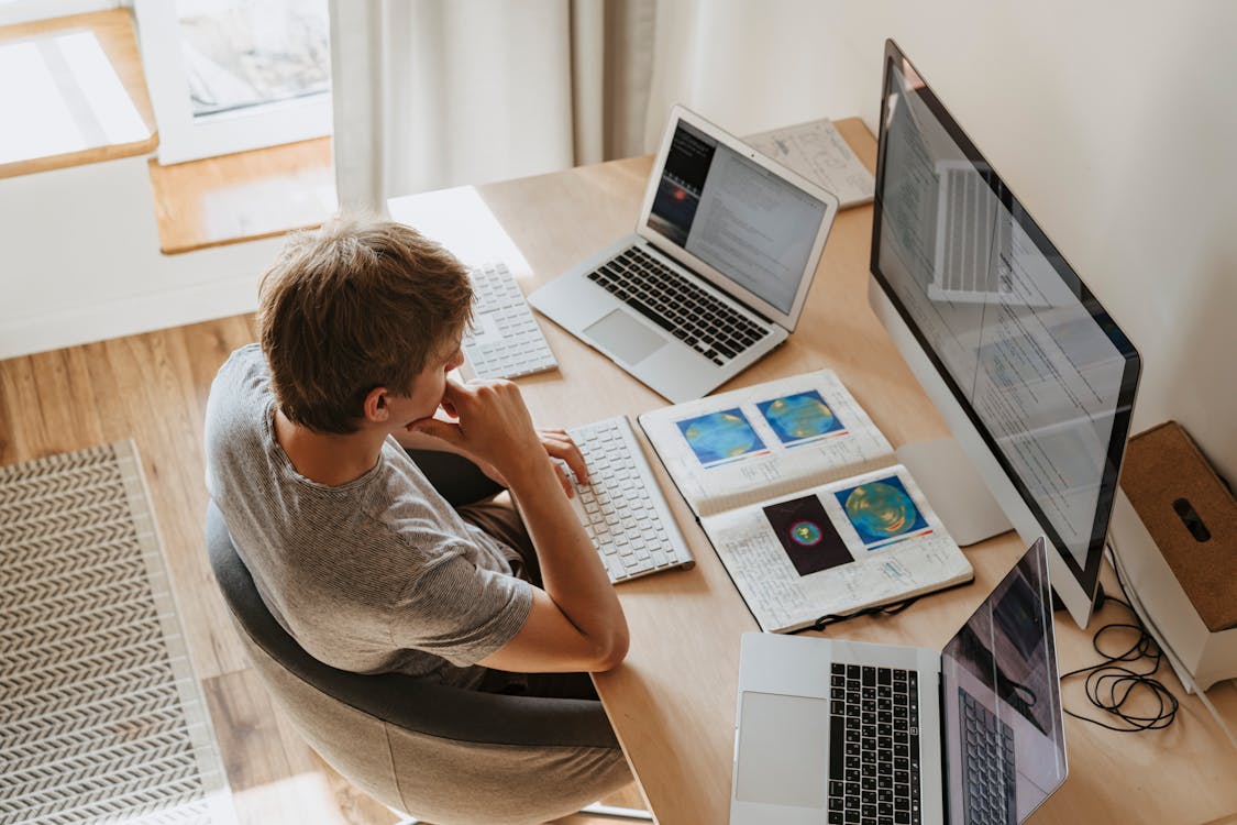 Man in Gray Crew Neck T-shirt Using Macbook Air on Brown Wooden Table