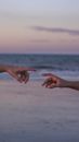 Crop unrecognizable couple of travelers reaching arms on sandy ocean shore under cloudy sky at sunset