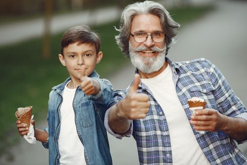 Free Grandfather and grandson enjoying ice cream and bonding outdoors with thumbs up. Stock Photo