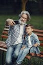 Man in Blue and White Plaid Dress Shirt Sitting on Brown Wooden Bench Beside Boy in during