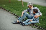 Man in Blue Denim Jeans Sitting Beside Girl in Gray Jacket on Gray Concrete Road during