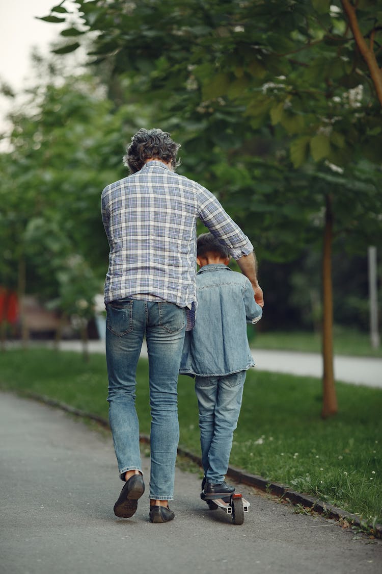 Back View Of Man Walking And Holding A Boy On A Skateboard