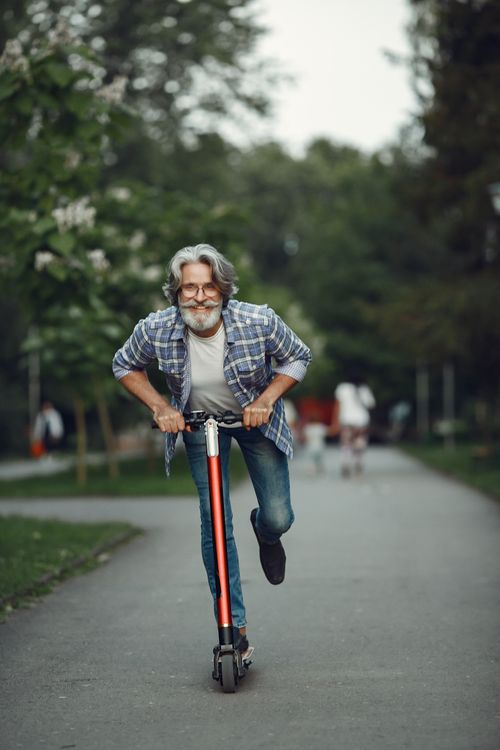 Free Elderly man joyfully riding a scooter on a park pathway during a sunny day. Stock Photo