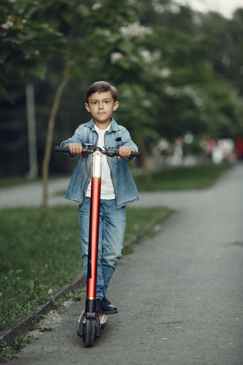 Free A boy rides his scooter in a park on a bright summer day, enjoying outdoor playtime. Stock Photo