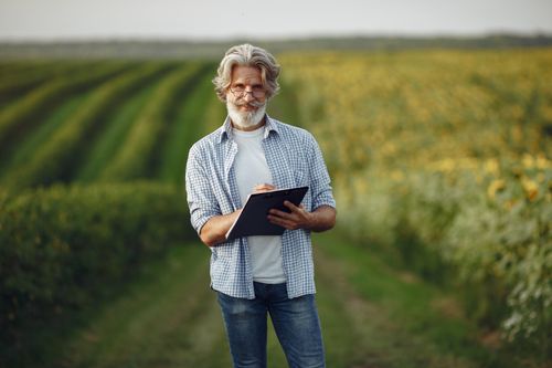 Free Senior farmer taking notes in sunny countryside field, wearing eyeglasses. Stock Photo