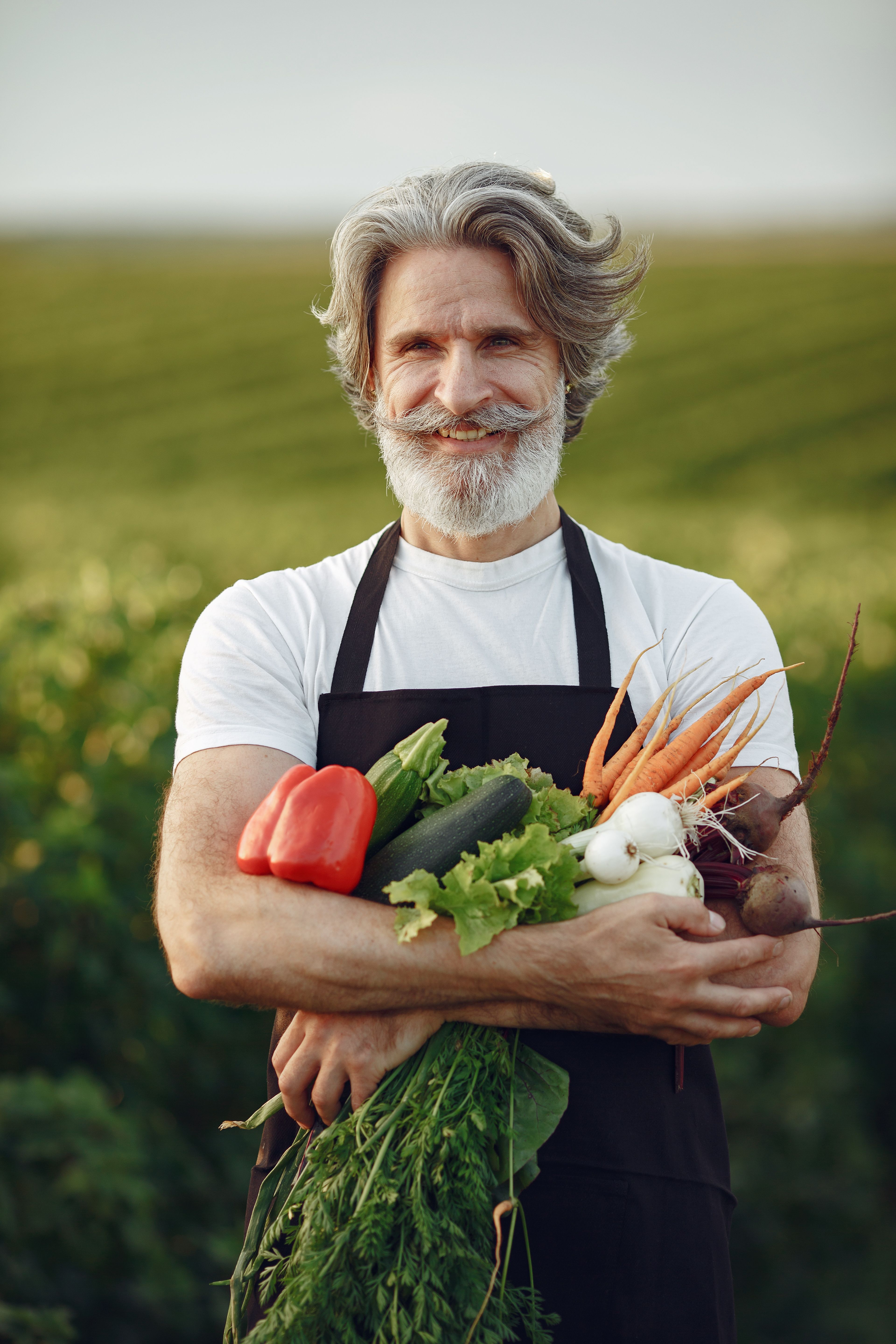 Senior grower smiling and holding a harvest of fresh vegetables