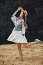 阳光明媚的乡村田野里，一位身穿白色连衣裙和牛仔夹克的女子正快乐地跳舞