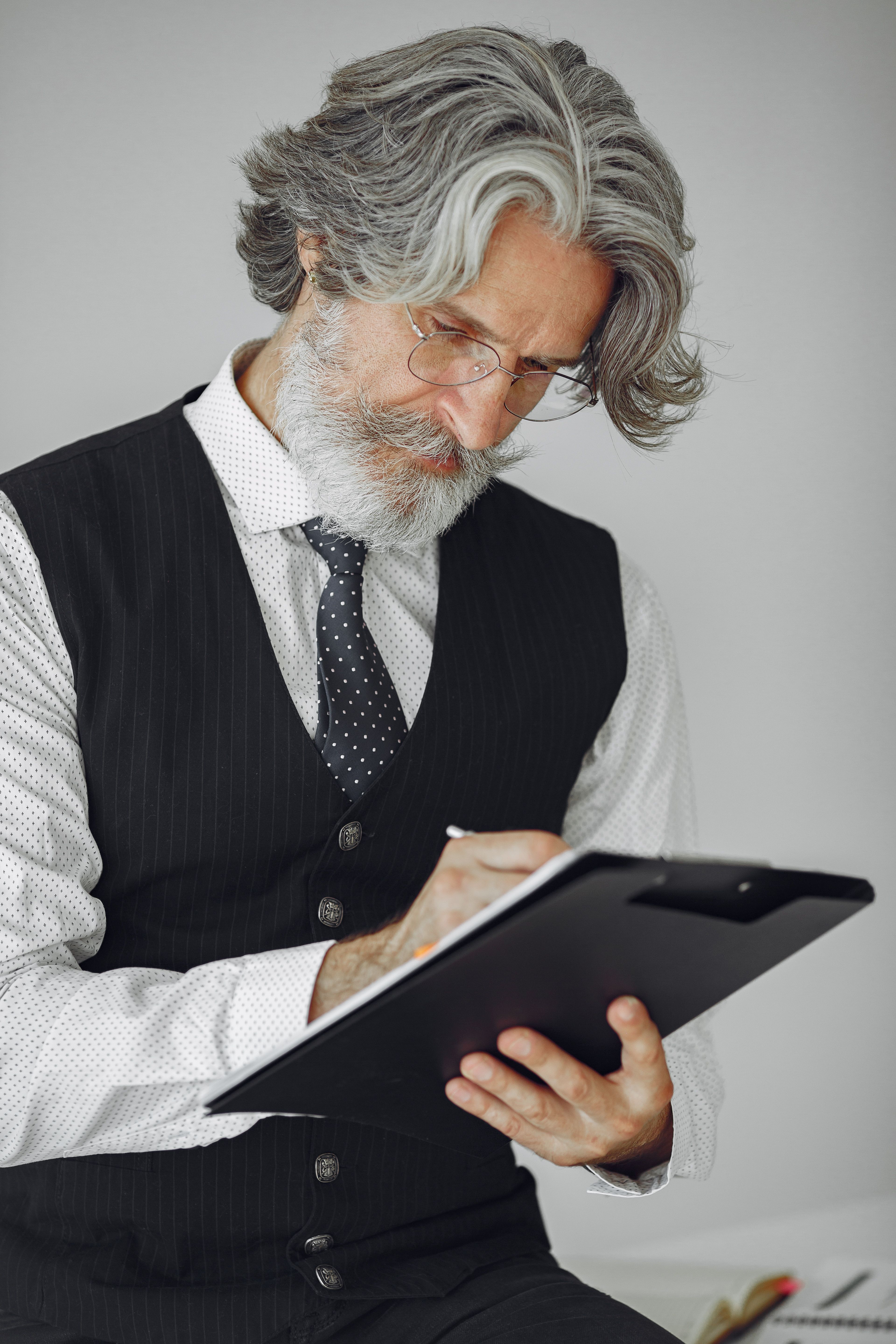 Stylish mature man in a suit writing on a clipboard in a professional office setting.