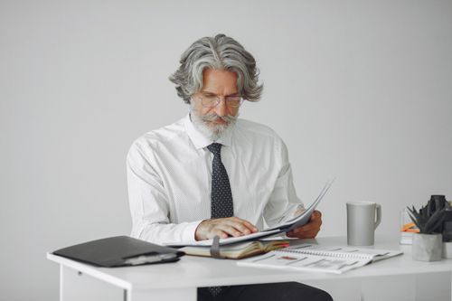 Free An elderly businessman reviewing documents at his desk in a modern office setting. Stock Photo