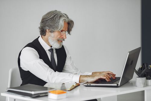 Free Elegant senior man in office attire typing on a laptop at a desk. Stock Photo