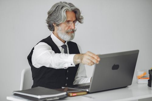 Free Senior man with gray hair working on a laptop in an elegant office setting, wearing a suit. Stock Photo
