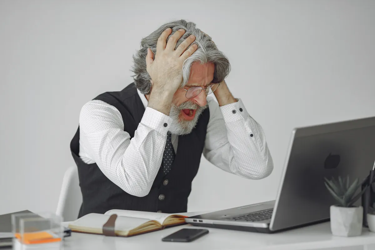Stressed man at a laptop, highlighting the need for an automated content creation tool to scale production.