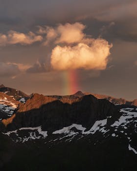 Stunning view of Norwegian mountains with a rainbow and cloud under a sunset sky.