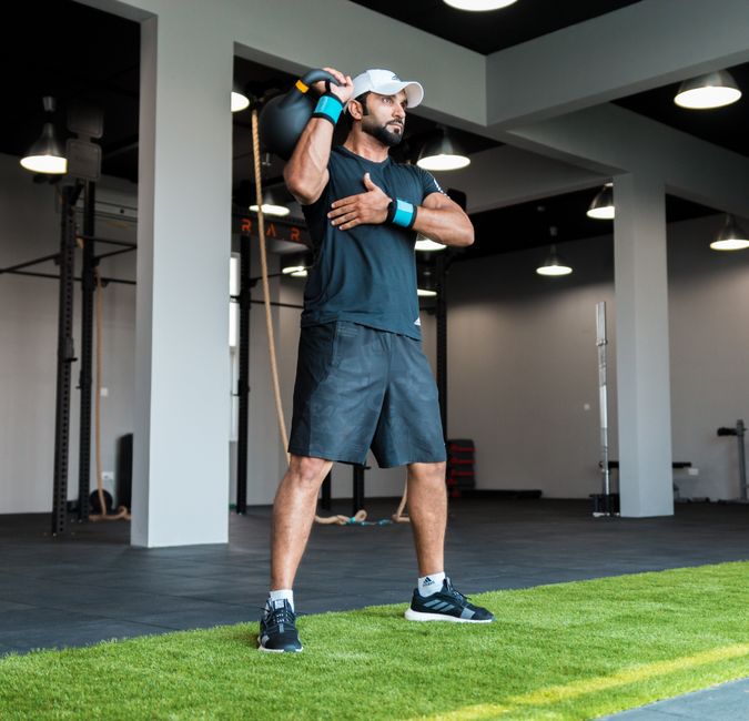 Man in activewear lifting a kettlebell indoors at a modern fitness center.