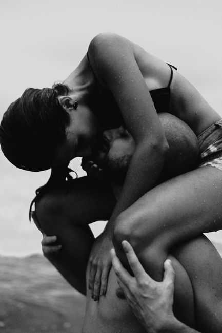A romantic black and white photo of a couple embracing playfully by the beach.