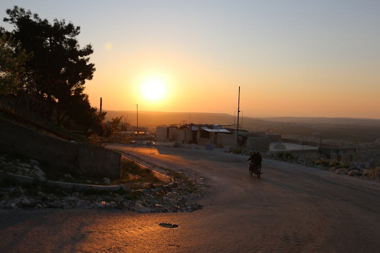 Unrecognizable Person Riding Motorcycle On Rural Road At Sunset