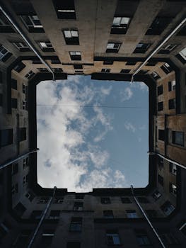 Low angle view of urban building square framing the bright blue sky and clouds.