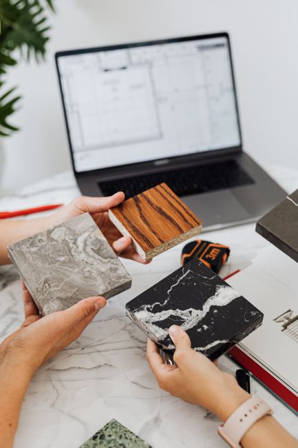 Photo by https://kaboompics.com/ on Pexels Hands assessing diverse tile samples on marble table with laptop plans.
