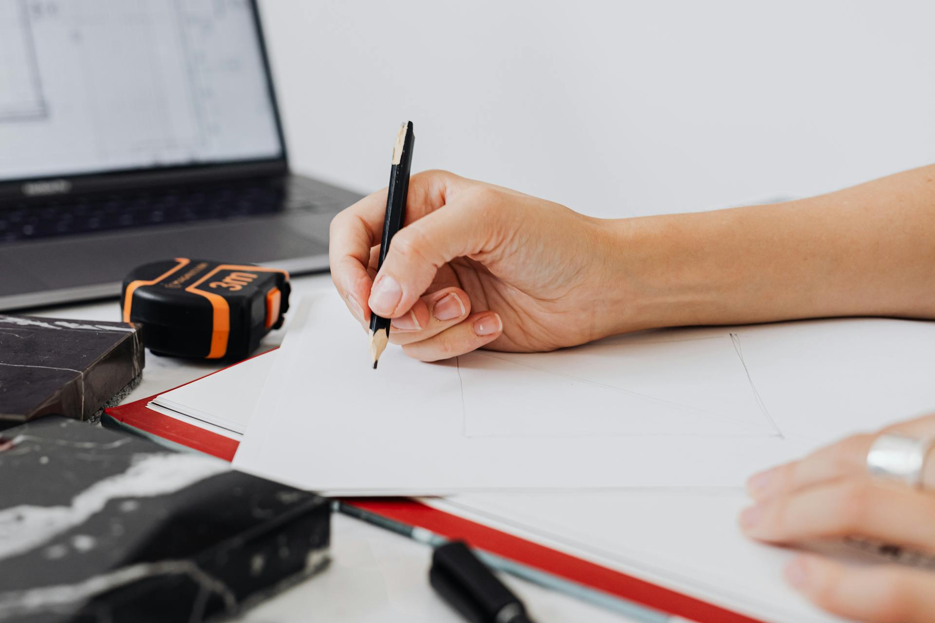 Close-up of a designer's hand sketching with a pencil on paper, illustrating architectural planning.