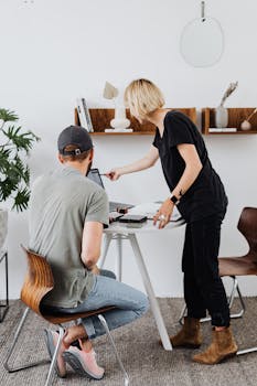 Two colleagues discuss a project at a desk in a stylish office setting.