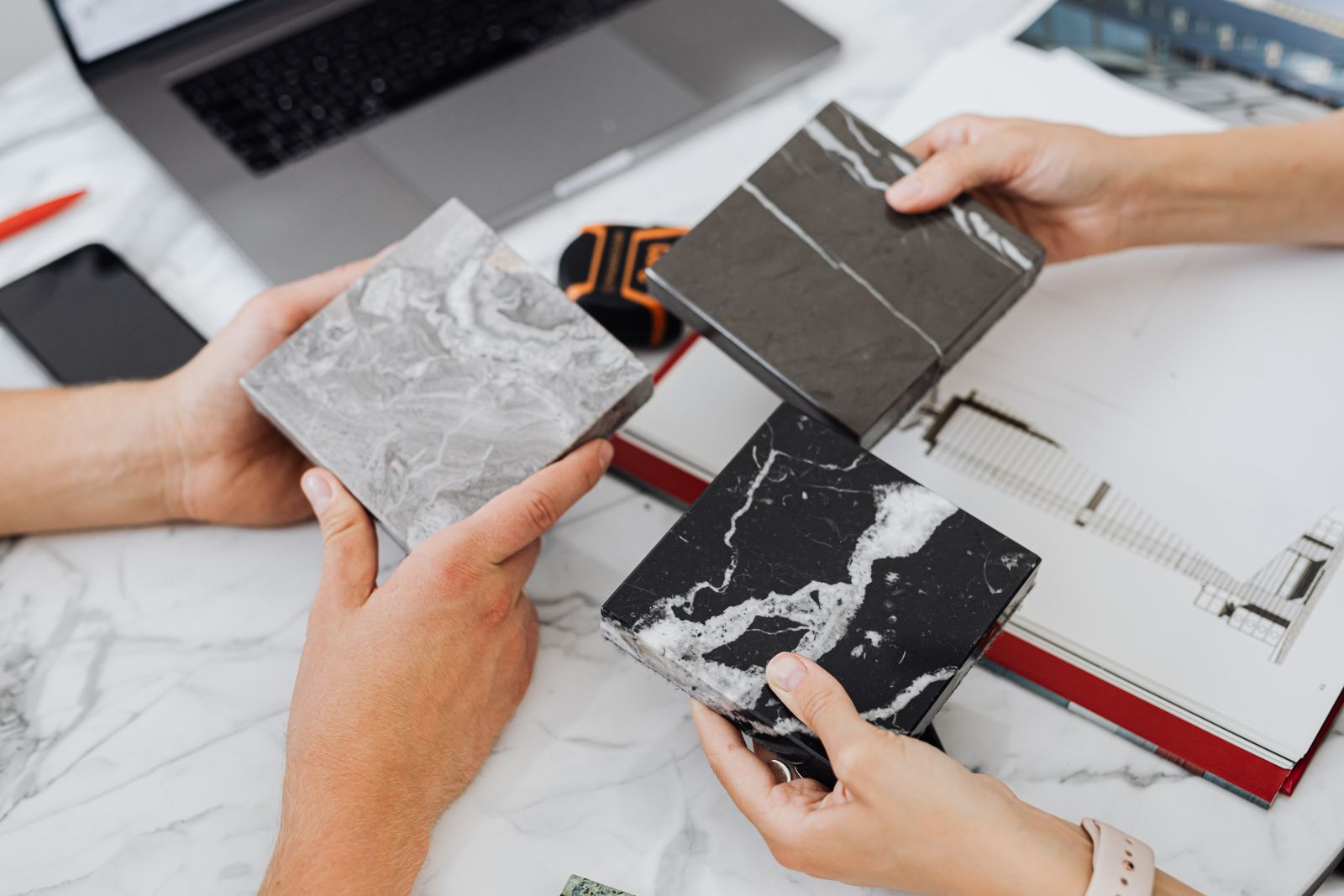 Two people comparing marble tile samples on a desk