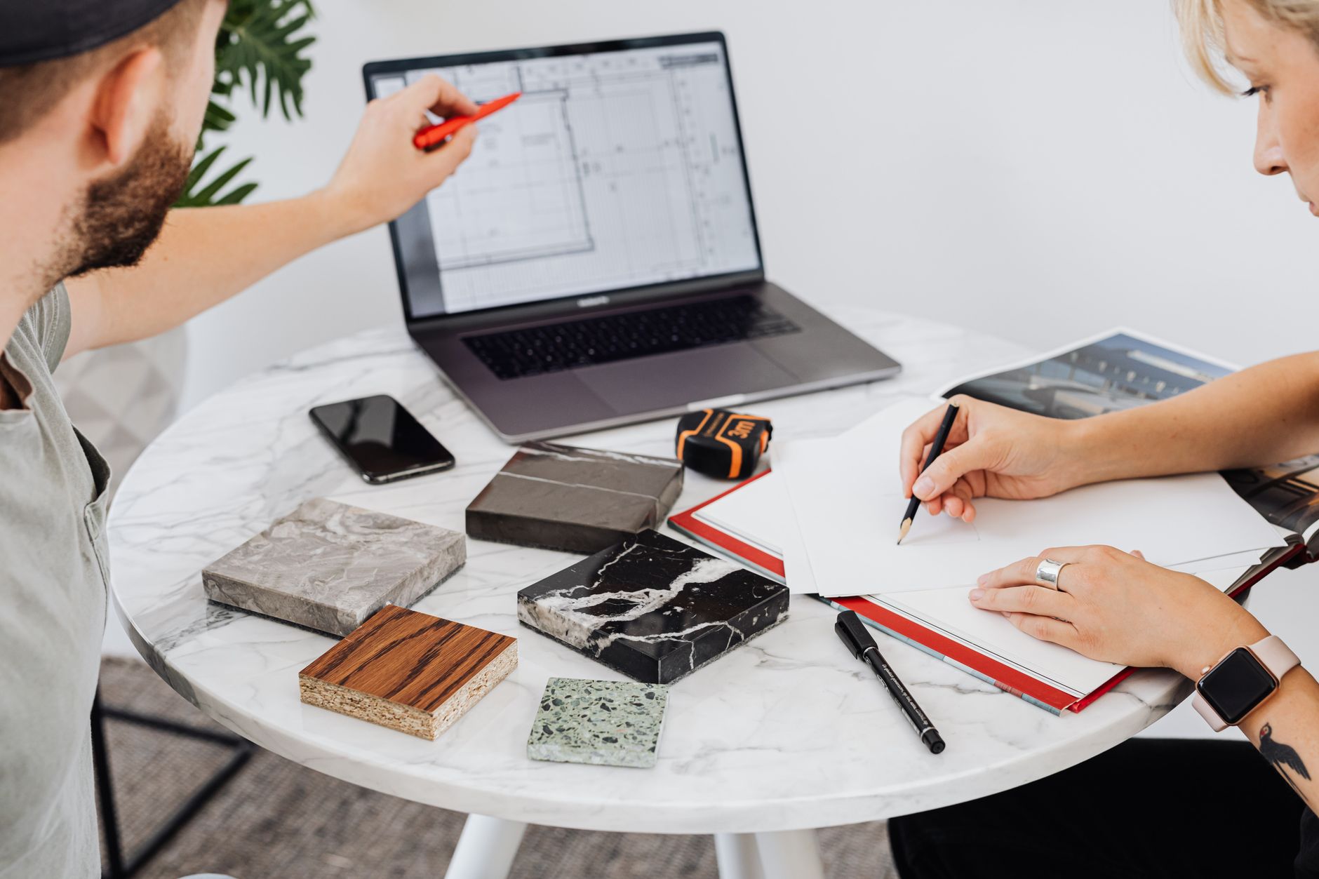 Deux designers collaborent sur un projet avec un ordinateur portable et des échantillons de matériaux sur une table en marbre.