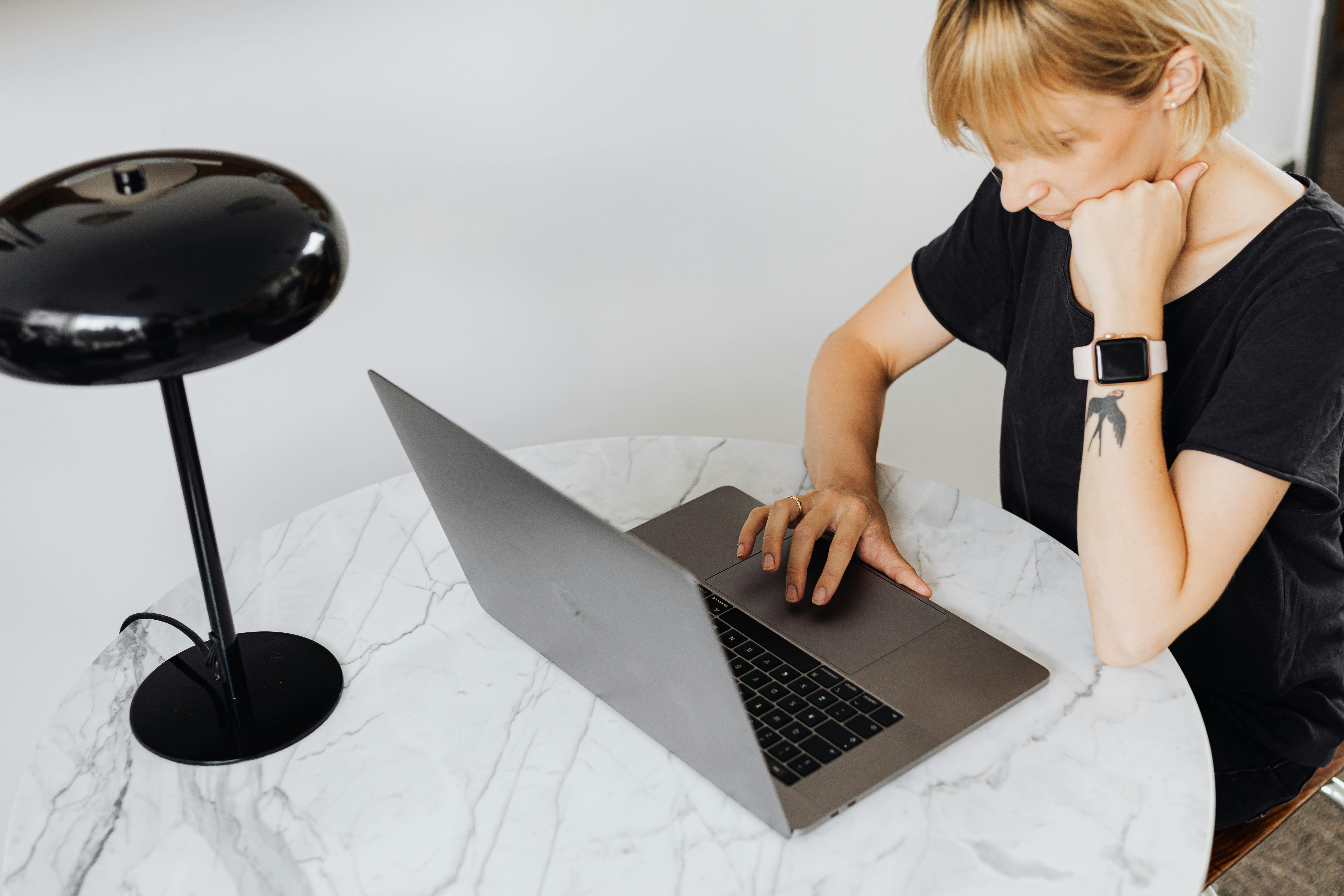 A focused woman works on her laptop at a marble table, showcasing tech-savvy lifestyle.