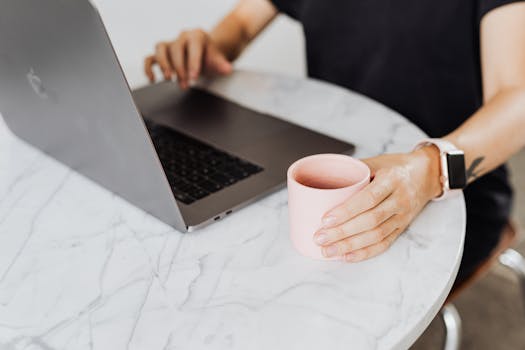 一个人在大理石桌子前，拿着咖啡杯，用笔记本电脑工作